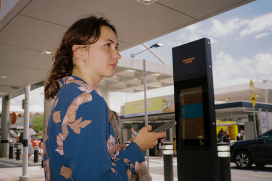 Woman using smartphone during commute in an outdoor transit hub. Film 