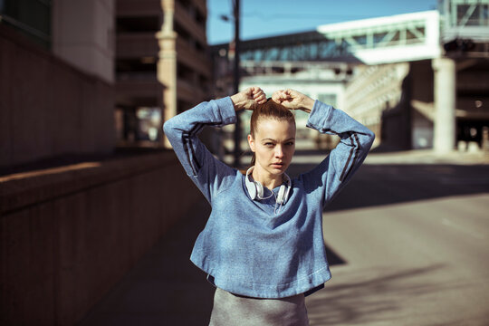 Focused female runner tying hair on urban street