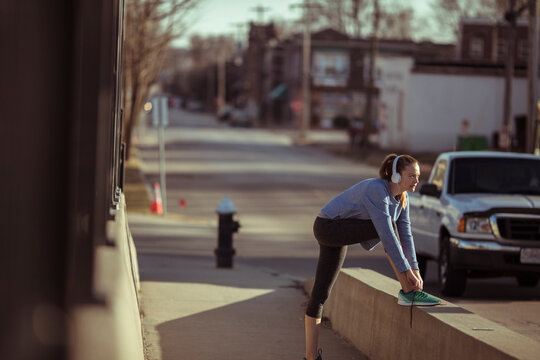 Young woman with headphones lacing running shoes on city sidewalk