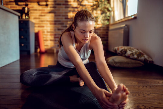 Young woman stretching on yoga mat at home