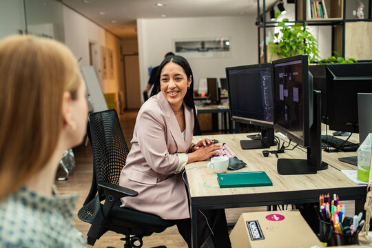 Smiling businesswoman talking with colleague at computer in modern office
