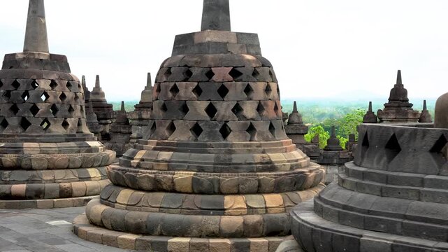 Waling around at stone Buddha statues seated inside perforated stupas at Borobudur temple in Java, Indonesia. Ancient Buddhist monument with multiple latticed stupas and spires