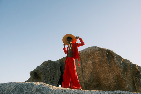 Young man in red clothing and straw hat posing on coastal rocks