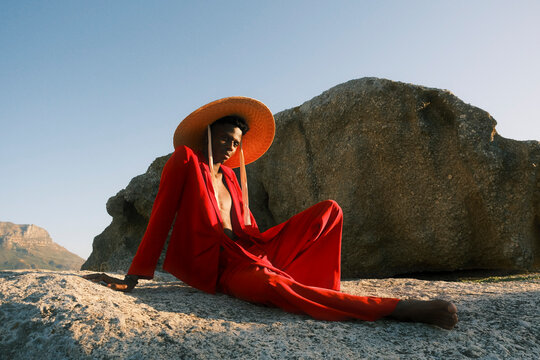 Young man in red clothing and straw hat sitting on coastal rocks