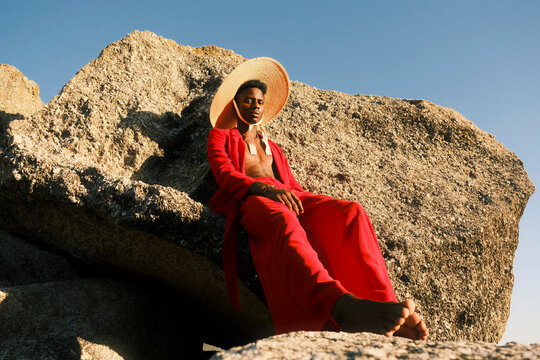 Young man in red clothing and straw hat sitting on coastal rocks