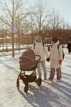Parents walk hand in hand with baby stroller in winter park
