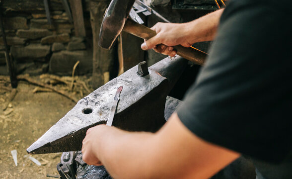 Craftsman forging knife blade on anvil in workshop