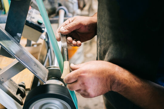 Craftsman sharpening blade on belt sander in workshop