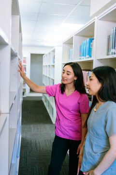 Classmates wearing scrubs browsing library shelves
