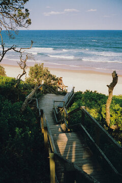 Woman with bodyboard on the steps to the sandy beach 