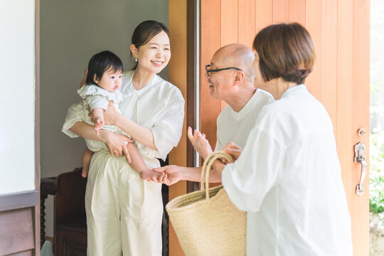 A daughter and granddaughter welcome their parents, who have come to visit or travel from the countryside, at the front door.