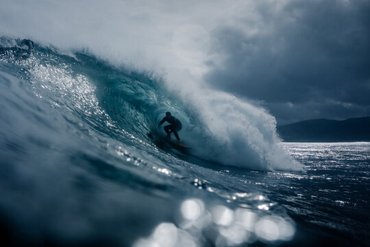 Surfer riding inside the hollow of a wave with thick clouds in the sky