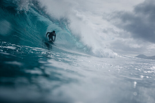 A pro surfer gliding through the barrel of a wave with cloudy skies