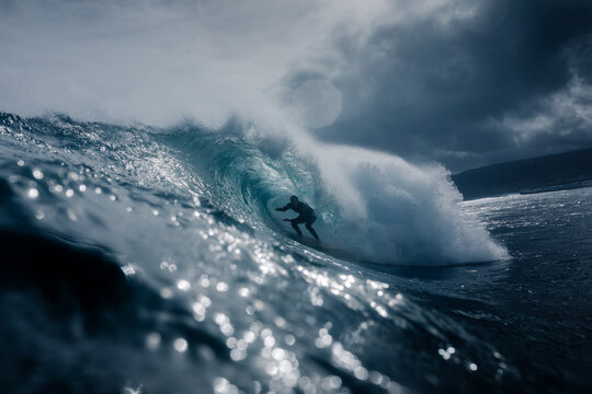 Surfer navigating through the hollow tube of a wave in cloudy weather