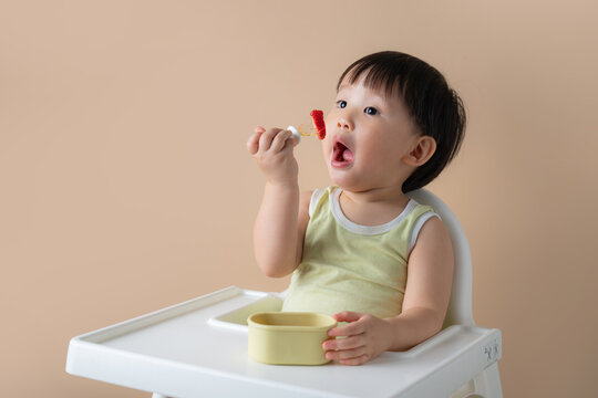 Adorable baby eating strawberry from fork while sitting in high chair