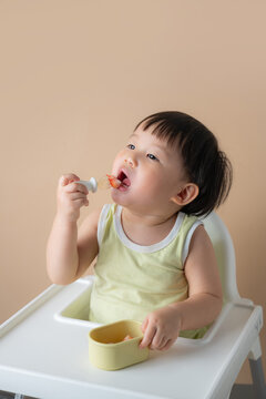 Adorable baby boy eating strawberry with a special baby spoon