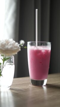Close-up of refreshing iced pink milk (Nom Yen) in a glass on a wooden table with a white flower in a vase, sweet beverage and lifestyle concept