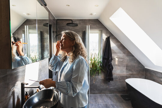 Woman applying makeup in front of a mirror in a modern bathroom