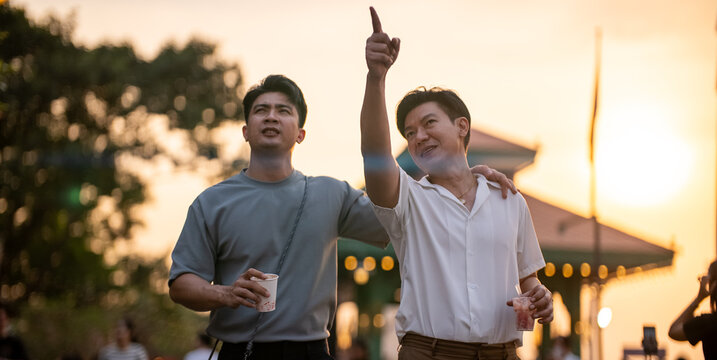 Asian gay couple enjoying sunset outing, pointing at buildings