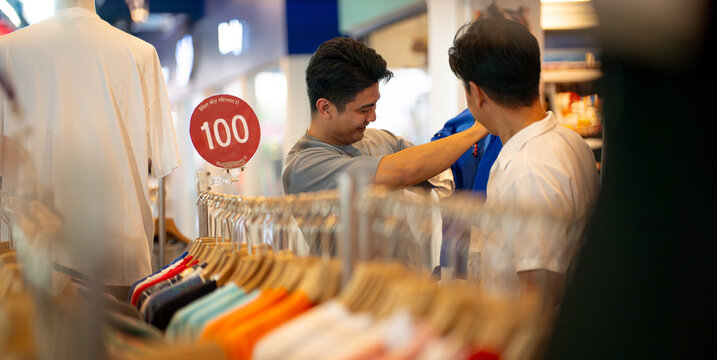 Two smiling men enjoy browsing clothes together on a mall in Bangkok