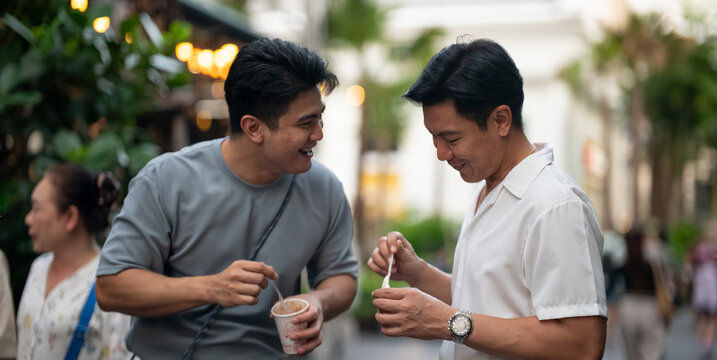Gay couple enjoying a sweet snack together smiling at an outdoor mall