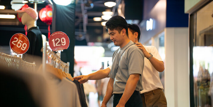 Gay couple shopping for clothes in modern mall enjoying quality time
