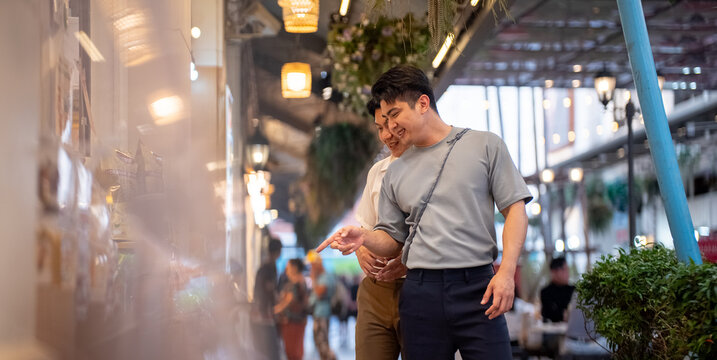 Gay couple enjoying shopping in urban market, pointing at buildings