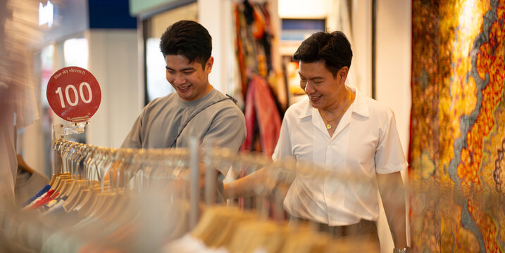 Gay couple enjoying retail shopping browsing clothes racks in mall