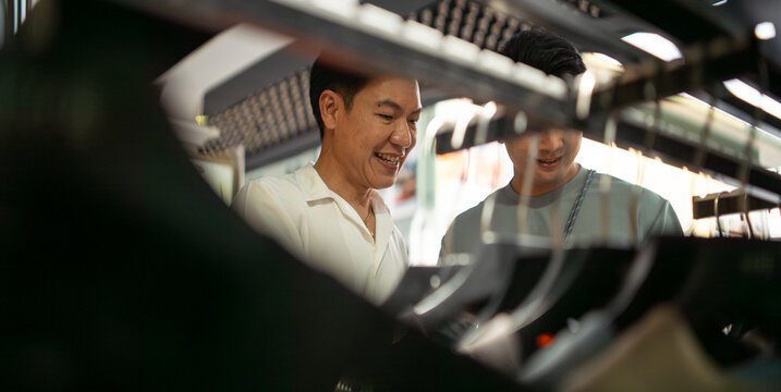 Smiling gay asian couple choosing clothes together at a modern mall