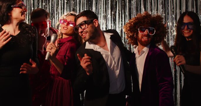 Karaoke party for happy friends, singer woman microphone singing with emotion, funny disco entertainment in club, laughing together to enjoy free time, metallic shiny glitter garland background
