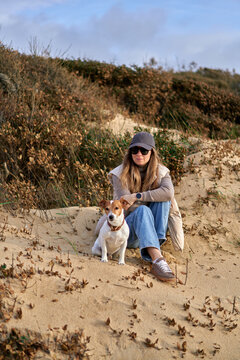Young Woman Sitting on Sand Dune With Her Dog Relaxing in Casual Autum
