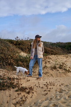 Young Woman Sitting on Sand Dune With Her Dog Relaxing in Casual Autum