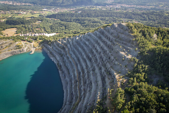Aerial view of Amiantifera di Balangero mine with its terraced rock formations and turquoise lake surrounded by lush green forests Balangero, Piedmont, Italy.