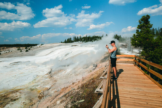 Visitor photographing steam vents from boardwalk in Yellowstone National Park