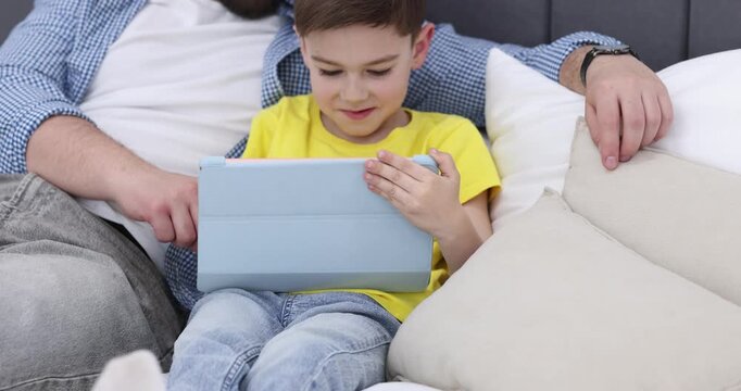 Father and his son using tablet on bed at home. Camera moving forward
