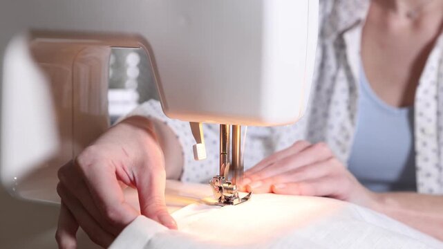 Woman sewing fabric with professional machine in workshop, closeup