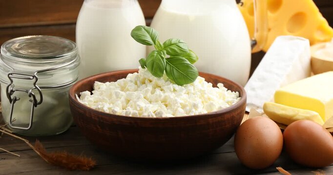 Woman putting basil leaves onto cottage cheese at wooden table with fresh dairy products, closeup