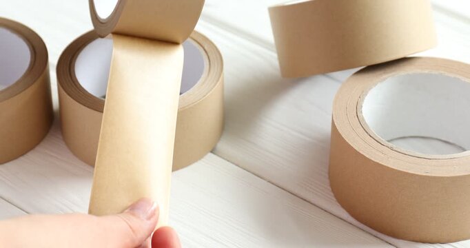 Eco-friendly packaging. Woman with rolls of masking tape at white wooden table, closeup