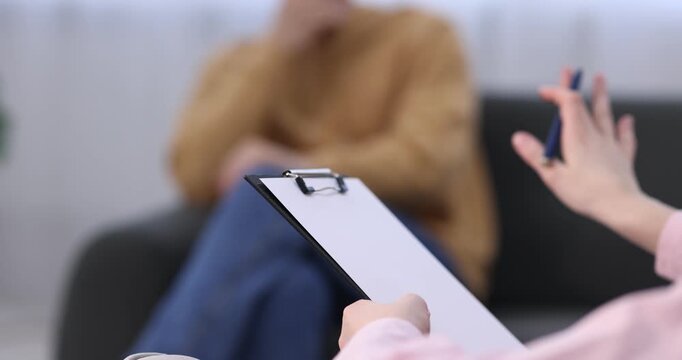 Professional psychologist with clipboard during therapy session with patient indoors, selective focus