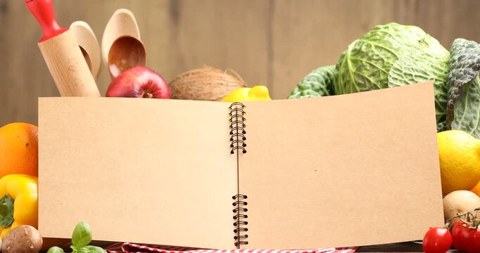 Open recipe book, kitchen utensils and fresh products on wooden table, closeup. Camera zooming in