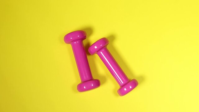 Pink dumbbells on yellow background, flat lay