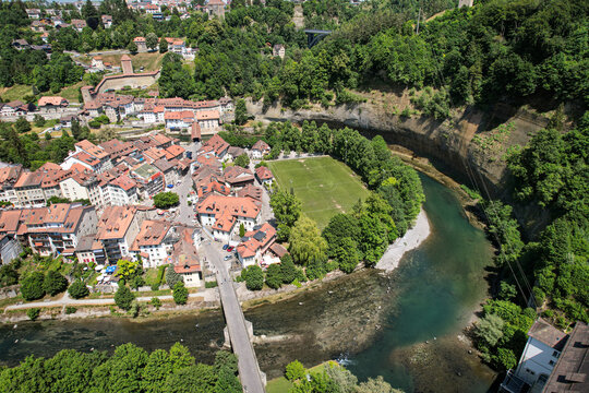 Aerial view of the historic old town with red-roofed houses, the Sarine river, and a green football pitch by the cliffs in Fribourg, Fribourg, Switzerland.