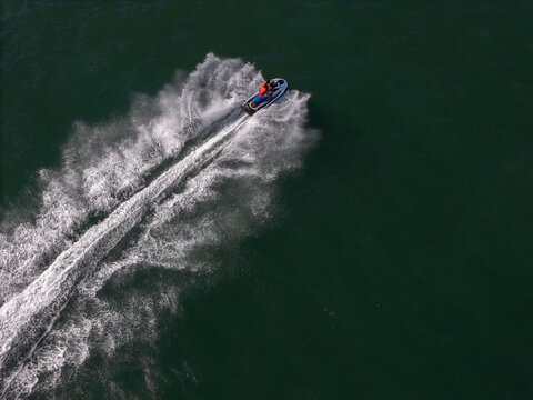 Aerial view of a person riding a jet ski at high speed across dark green water with a large white wake.