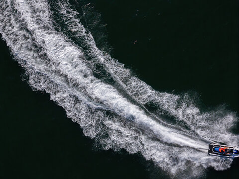 Aerial view of a person riding a jet ski across dark deep water leaving a large white foamy wake.