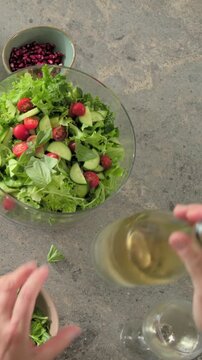 Vertical video: Entering overhead, cook tearing basil and pouring oil over salad bowl on counter
