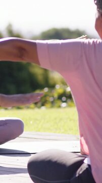 Vertical video: Stretching senior pink top opening arms forward on deck  and  mats bottles, copy spa