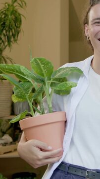 Vertical video: Recording person wearing white T-shirt presenting clay pot in doorway showing plant