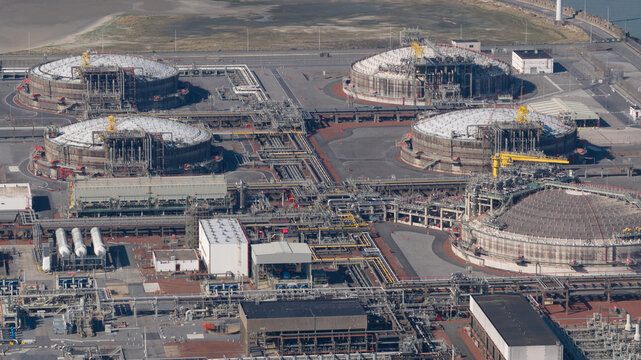 Aerial view of the Fluxys LNG Terminal Zeebrugge with large circular storage tanks and complex industrial piping systems in Brugge, Vlaanderen, Belgium.