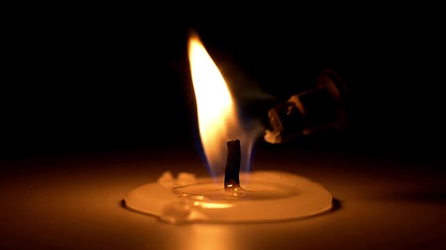 A warm light flickers from a single candle flame against a dark background