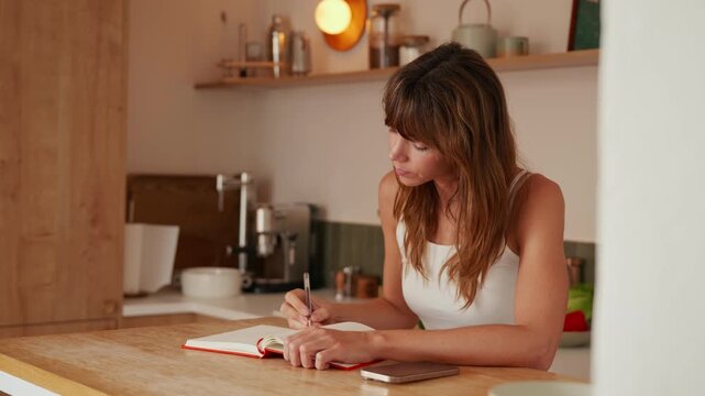 Thoughtful Woman Writing Notes and Planning in Her Kitchen